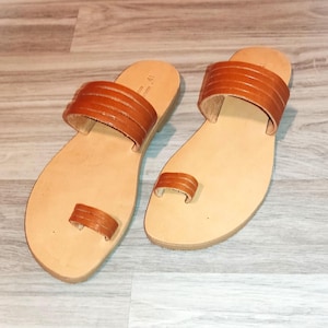 May include: A pair of brown leather sandals with a toe ring and two straps across the top of the foot.