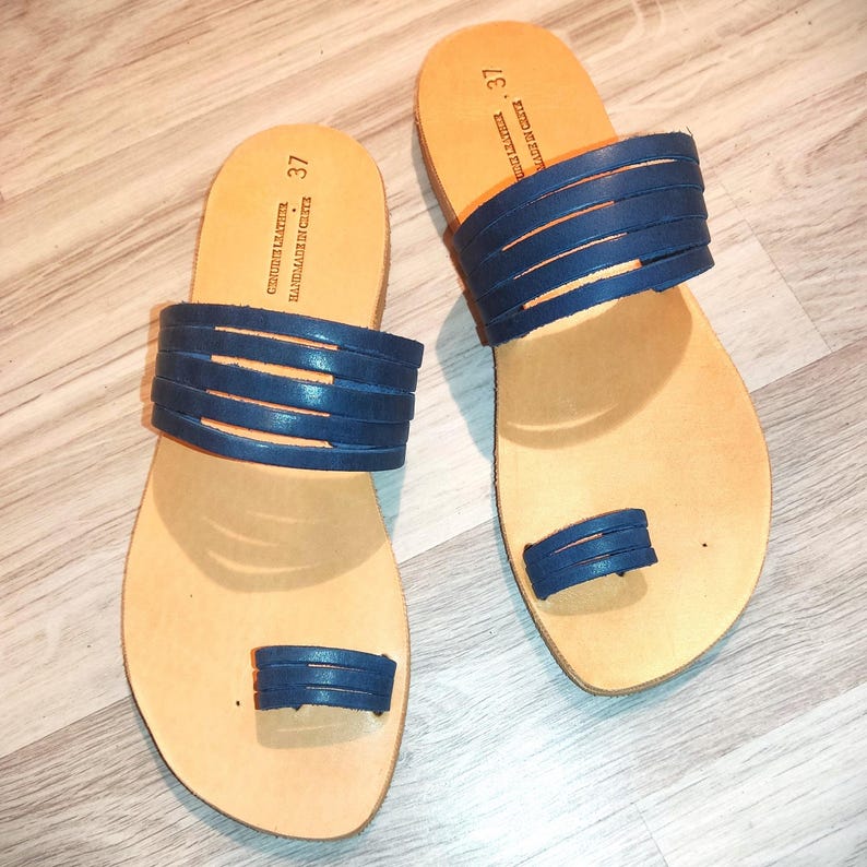May include: A pair of blue leather sandals with a toe ring. The sandals are handmade in Crete and are size 37.