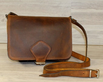 May include: A brown leather crossbody bag with a flap closure and a silver buckle. The bag has a long adjustable strap.
