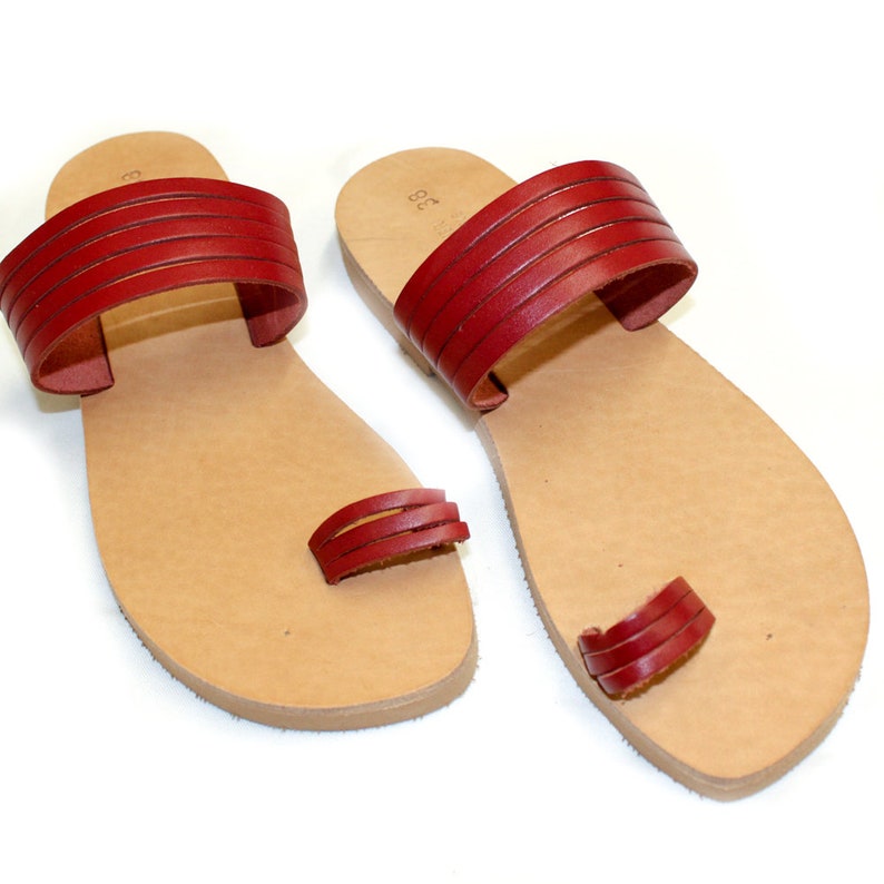 May include: A pair of red leather sandals with a toe loop and a strap across the top of the foot. The sandals have a brown leather sole.