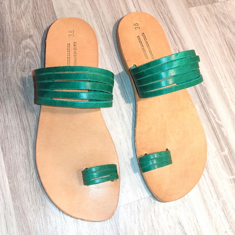 May include: A pair of green leather sandals with a toe ring and multiple straps. The sandals are size 38.