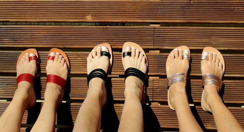 May include: Five pairs of leather sandals with different colored straps. The sandals are all brown leather with a toe loop and a strap across the foot. The straps are black, red, silver, gold, and white.
