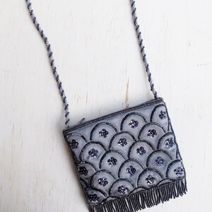 Puede incluir: Un bolso de noche gris con cuentas, con una correa de cadena plateada y un dise&ntilde;o de concha. El bolso tiene un ribete de flecos.