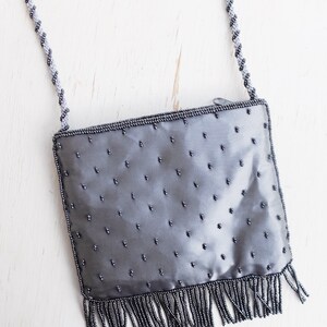 Puede incluir: Un bolso de noche gris con cuentas, con ribete de flecos y una correa de cadena plateada.