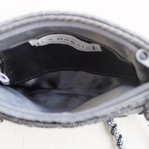 Puede incluir: Un bolso de noche gris con cuentas, con cierre de cremallera y una correa de cuentas negras y grises. El bolso tiene un forro de sat&eacute;n negro y una peque&ntilde;a etiqueta blanca en el interior que dice "La Regale".