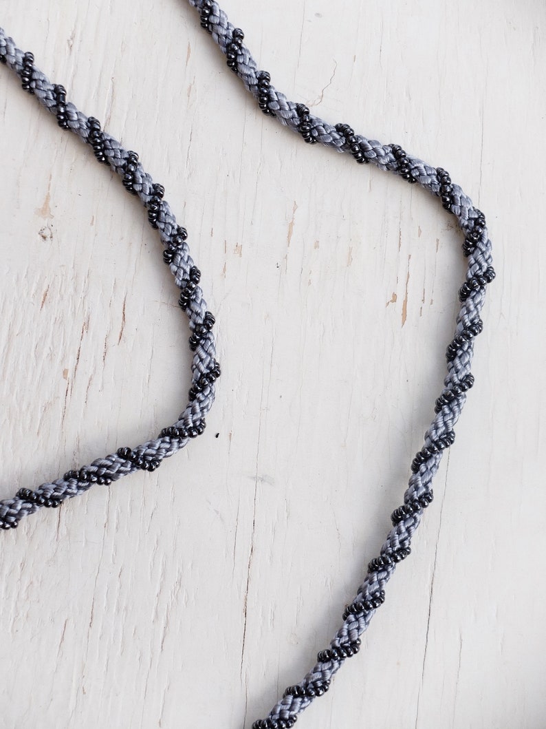 Puede incluir: Un collar de cord&oacute;n trenzado gris y negro con un dise&ntilde;o trenzado.