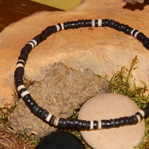 Può includere: Una collana di perline in legno nero e bianco. La collana è su una superficie di legno con muschio e pietre.