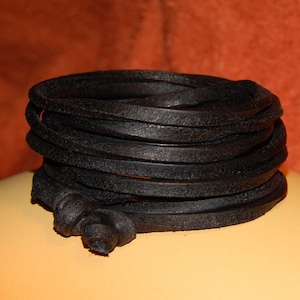 May include: A coiled black leather cord, possibly for jewelry or crafts, is the central focus. The cord is tightly wound, with a textured surface. The background is a blurred orange and yellow.