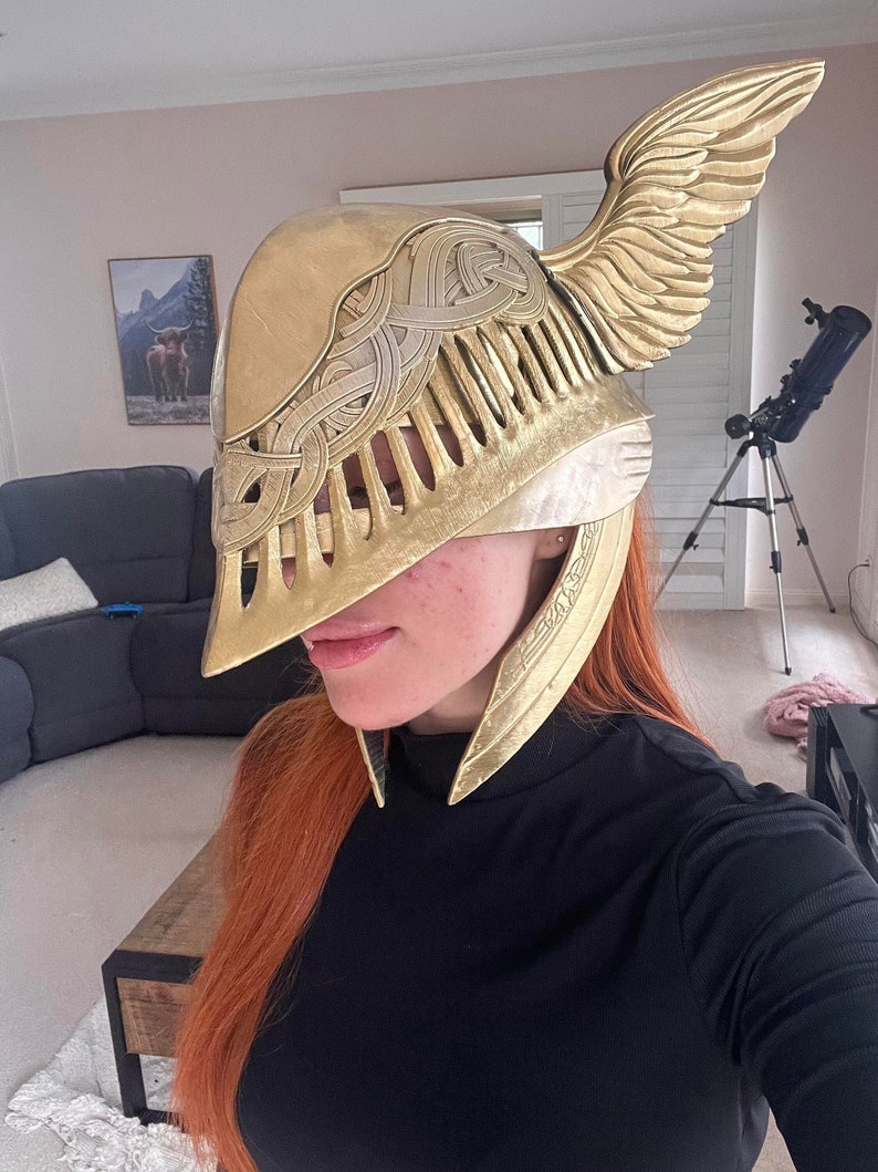K&ouml;nnte beinhalten: Ein goldfarbener Helm mit filigranen Details und einem Fl&uuml;geldesign. Der Helm ist aus leichtem Material gefertigt und hat einen schlanken, modernen Look.