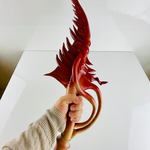May include: A red and orange decorative sword with a unique, organic design. The sword has a curved blade with a series of spikes and a handle that resembles a twisted vine.