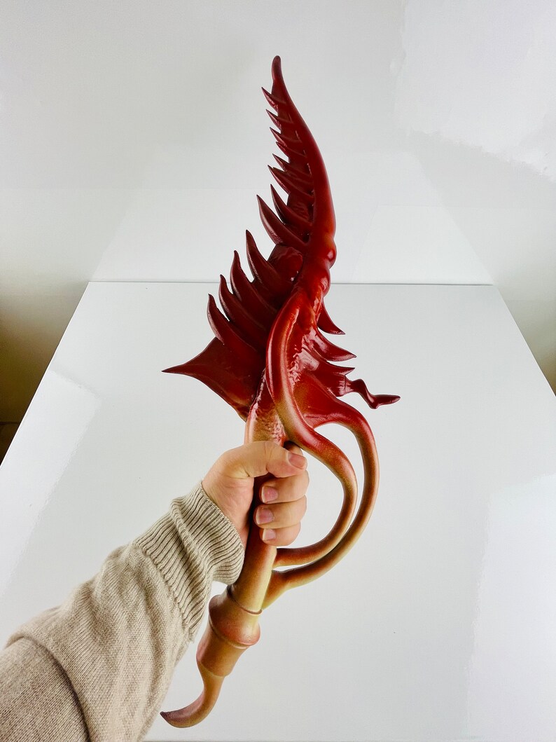 May include: A red and orange decorative sword with a unique, organic design. The sword has a curved blade with a series of spikes and a handle that resembles a twisted vine.