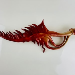 May include: A red and brown, organic-shaped, decorative sculpture with a spiky, jagged edge and a curled, tubular end.