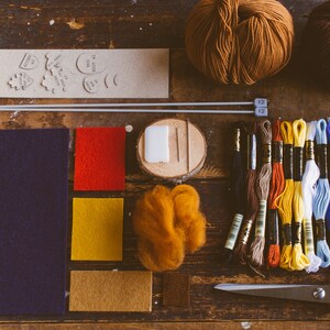 Tools and materials needed to make the bookmark gathered on the dark wood table: felt, needles, scissors, hreads, yarn, pattern and chalk