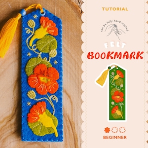 Puede incluir: Un marcapáginas de fieltro azul con flores de capuchina naranjas y hojas verdes bordadas, terminado con una borla amarilla. La imagen incluye el texto TUTORIAL, can be fully hand-stitched, FELT BOOKMARK, BEGINNER y una versión en verde.