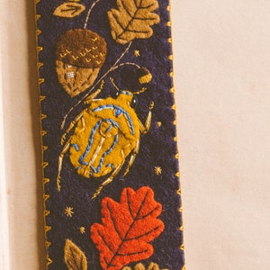 Felt bookmark featuring the applique of the bug, oak leaves and acorns shown against book spread.