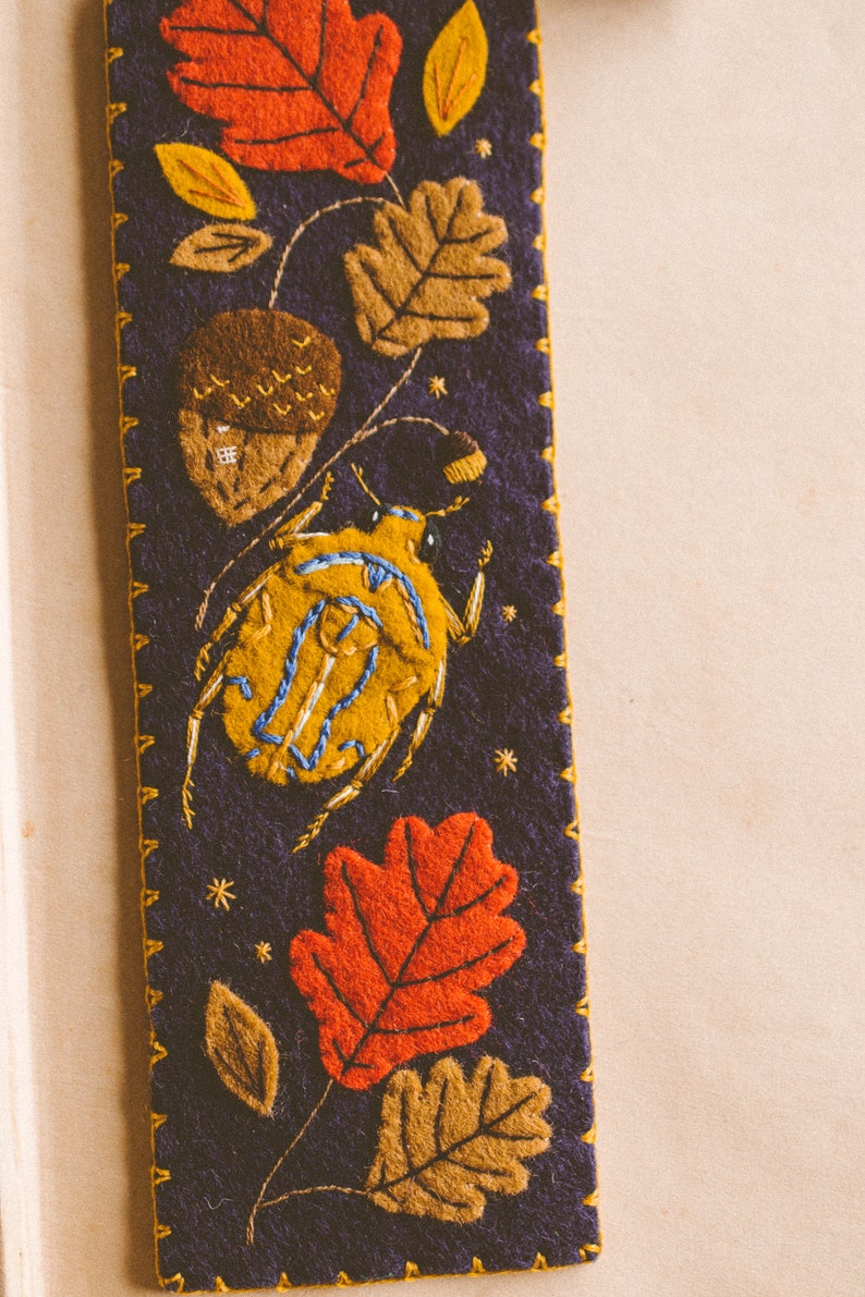 Felt bookmark featuring the applique of the bug, oak leaves and acorns shown against book spread.