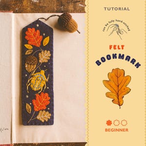 Pode incluir: Marcador de livros de feltro feito à mão com folhas de outono bordadas, bolotas e um besouro em um fundo azul escuro. O marcador de livros é preso a uma bolota marrom. O texto "FELT BOOKMARK" e "BEGINNER" também são visíveis.