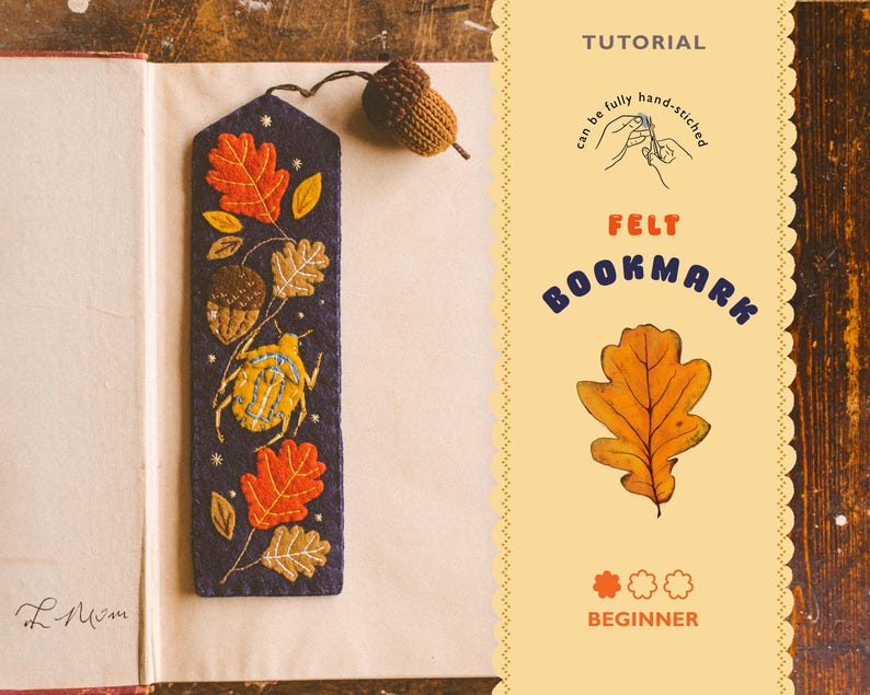 May include: A handmade felt bookmark with embroidered autumn leaves, acorns, and a beetle on a dark blue background. The bookmark is attached to a brown acorn. The text "FELT BOOKMARK" and "BEGINNER" are also visible.