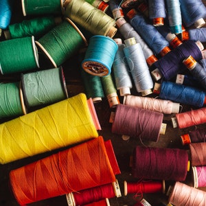 May include: A collection of colourful spools of thread in various shades of blue, green, red, yellow, and brown. The spools are arranged in a random pattern on a wooden surface.