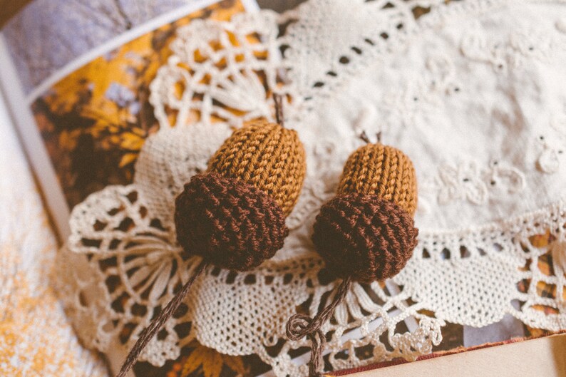 Two bookmark acorn charms as shown against white retro doily