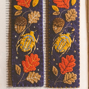 Two felt bookmark featuring the applique of the bug, oak leaves and acorns shown against book spread.