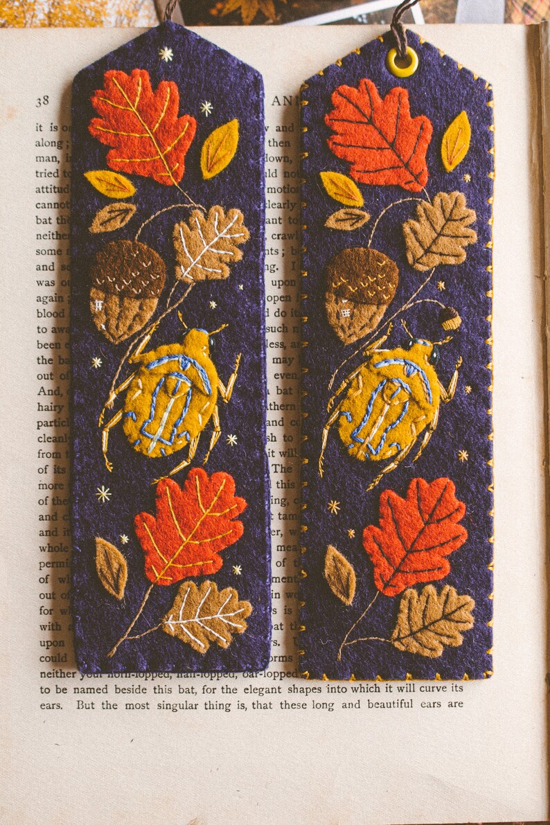Two felt bookmark featuring the applique of the bug, oak leaves and acorns shown against book spread.