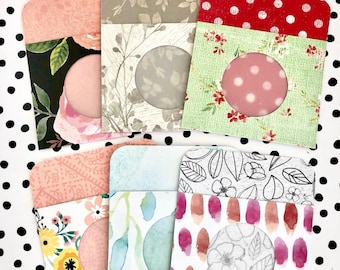 May include: Six different patterned paper gift card holders with a round window for a gift card. The holders are all different colors and patterns, including floral, polka dot, and watercolor.