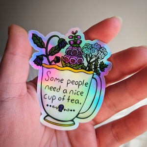 May include: A holographic sticker with a teacup and flowers. The teacup has a yellow rim and the text "Some people need a nice cup of tea." The flowers are purple, blue, and green.