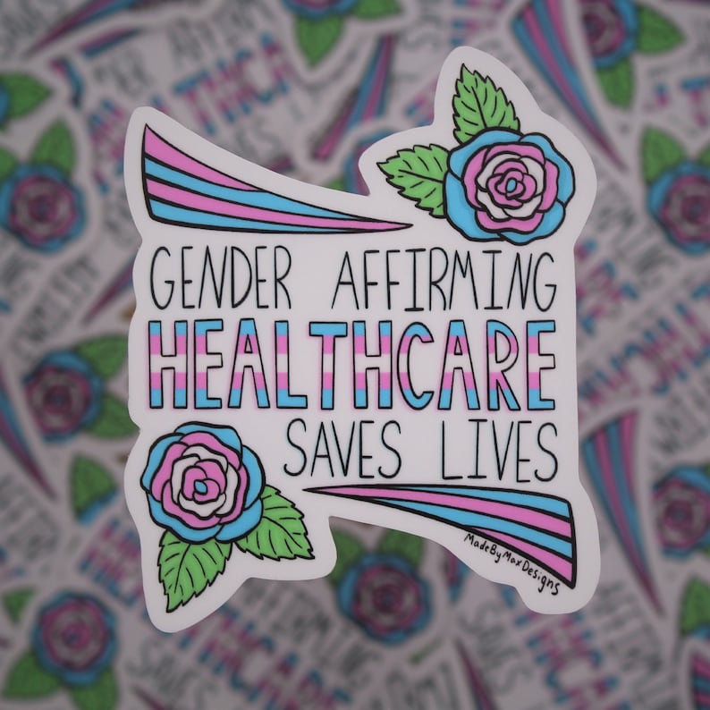 Pu&ograve; includere: Un adesivo bianco con un design a strisce rosa, blu e azzurro. L'adesivo presenta due rose stilizzate con foglie verdi e il testo "Gender Affirming Healthcare Saves Lives". Il testo "MadeByMaxDesigns" &egrave; nell'angolo in basso a destra.