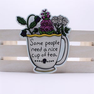May include: A white teacup with a yellow rim and a handle, filled with purple and white flowers. The text "Some people need a nice cup of tea." is written on the cup.