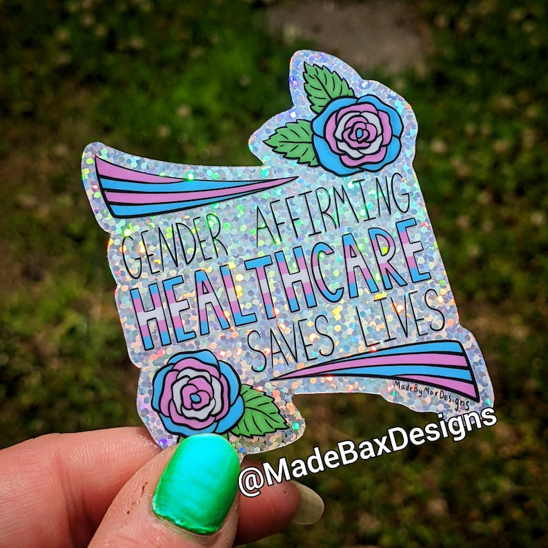Pu&ograve; includere: Un adesivo scintillante e iridescente con il testo "Gender Affirming Healthcare Saves Lives" in uno schema di colori arcobaleno. L'adesivo presenta due rose stilizzate con petali rosa, blu e bianchi.
