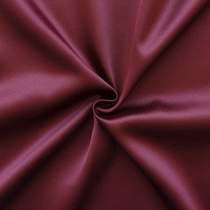 Könnte beinhalten: Nahaufnahme eines glatten, tief burgunderfarbenen Stoffes mit weicher, seidenartiger Textur. Der Stoff ist gefaltet und drapiert und erzeugt einen luxuriösen und eleganten Look.