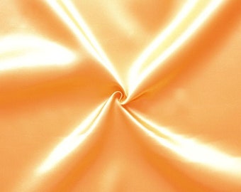 May include: A close-up of a smooth, silky fabric in a light orange color. The fabric is folded and draped, creating soft, flowing lines.