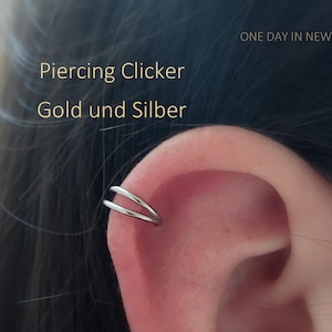 Könnte beinhalten: Ein silberner Piercing-Clicker-Ohrring wird an einem Ohr gezeigt. Der Text "Piercing Clicker Gold und Silber" ist in goldfarbenen Buchstaben dargestellt. Die Worte "ONE DAY IN NEW YORK" stehen oben rechts.