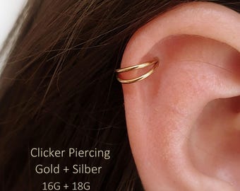 Puede incluir: Un anillo de piercing tipo clicker doble de color dorado colocado en el cartílago superior de la oreja. El texto en la imagen dice: Clicker Piercing, Gold + Silber, 16G + 18G, ONE DAY IN NEW YORK. La joya tiene un acabado liso y pulido.