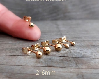 Puede incluir: Pendientes de botón con forma de bola dorada en varios tamaños de 2-6mm. El texto en la imagen dice ONE DAY IN NEW YORK, EDELSTAHL/HYPOALLERGEN, 2-6MM y GOLD/SILBER. Los pendientes cuentan con una cabeza esférica pulida y un poste.