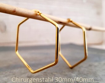 Puede incluir: Un par de pendientes de aro hexagonales de color dorado hechos de acero quirúrgico. Los pendientes cuelgan de una fina varilla de madera. El texto en la imagen dice Chirurgenstahl 30mm/40mm y ONE DAY IN NEW YORK.