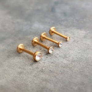 Puede incluir: Cuatro anillos de labio de color dorado con piedras de cristal transparentes. Los anillos est&aacute;n dispuestos en orden de tama&ntilde;o, con el anillo m&aacute;s peque&ntilde;o a la izquierda y el anillo m&aacute;s grande a la derecha.