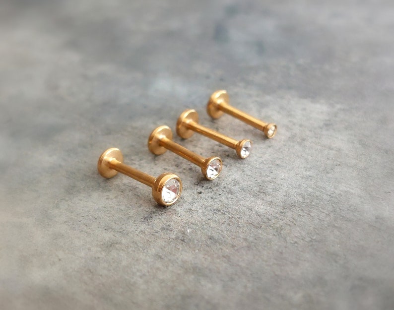 Puede incluir: Cuatro anillos de labio de color dorado con piedras de cristal transparentes. Los anillos est&aacute;n dispuestos en orden de tama&ntilde;o, con el anillo m&aacute;s peque&ntilde;o a la izquierda y el anillo m&aacute;s grande a la derecha.