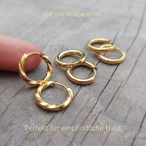 Könnte beinhalten: Goldfarbene Creolen mit gedrehter Textur. Das Set enthält mehrere kreisförmige Ohrringe mit einem Klappverschluss. Der Text "ONE DAY IN NEW YORK" und "Perfekt für empfindliche Haut" ist auf dem Bild zu sehen.