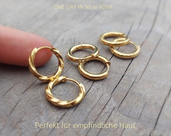 Puede incluir: Pendientes de aro dorados con textura trenzada. El conjunto incluye varios aros circulares con un mecanismo de cierre de bisagra. El texto "ONE DAY IN NEW YORK" y "Perfekt für empfindliche Haut" es visible en la imagen.
