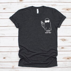 May include: Dark gray t-shirt featuring a white cartoon ghost with sunglasses making a peace sign. The ghost has a simple, minimalist design. The shirt has a crew neck and short sleeves.