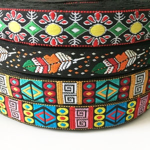 Puede incluir: Una pila de cuatro rollos de cinta tejida negra, cada uno con patrones bordados distintos. Los diseños incluyen motivos florales coloridos, formas de plumas estilizadas y patrones geométricos de diamantes y cuadrados en rojo, amarillo, verde y azul.
