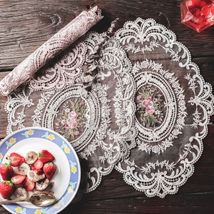 May include: Two white lace tablecloths with floral embroidery. The lace is delicate and intricate, with a scalloped edge. The tablecloths are perfect for adding a touch of elegance to any table setting.