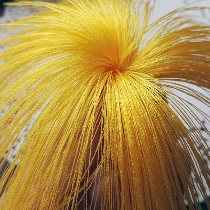 May include: A close-up of a bright yellow, fluffy, yarn pom-pom. The yarn is tightly wound and creates a radial pattern.