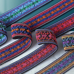 Könnte beinhalten: Mehrere Streifen aus gewebtem elastischem Band mit komplizierten geometrischen Mustern in leuchtenden Farben wie Hellblau, Orange, Pink, Violett und Grün, alle auf schwarzem Hintergrund mit schwarz eingefassten Kanten.