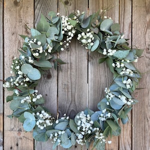 May include: A green eucalyptus and white baby's breath wreath hanging on a wooden fence.