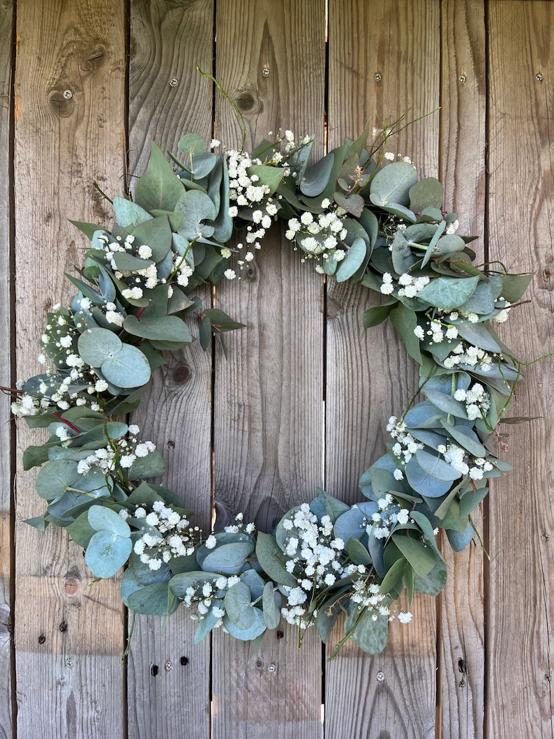 May include: A green eucalyptus and white baby's breath wreath hanging on a wooden fence.