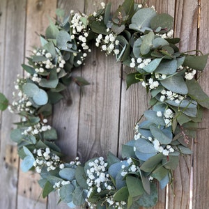 May include: A green eucalyptus wreath with white baby's breath flowers.