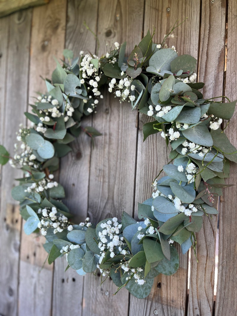 May include: A green eucalyptus wreath with white baby's breath flowers.